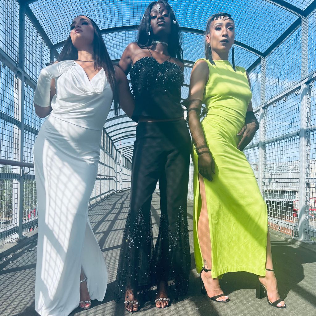 Landscape photograph of three women wearing a rented white grecian dress, black bejewelled co-ord two piece set and a lime green backless evening dress 